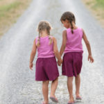 Two young girls holding hands walking down road