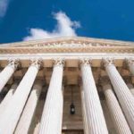 A low-angle view of a grand classical building with tall, white columns and a pedimen