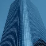 A dramatic low-angle shot of a tall, modern, curved building with a grid of blue reflective windows.