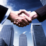 Two business people shaking hands against a background of modern city skyscrapers.