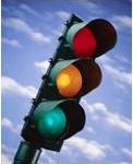 A three-color traffic light is shown against a blue sky with white clouds.