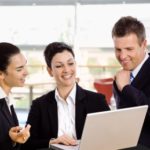 Three colleagues laughing while looking at a laptop.
