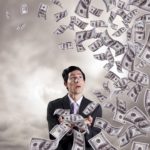 A man in a suit looking at a bunch of bills flying in the air