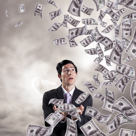 A man in a suit looking at a bunch of bills flying in the air