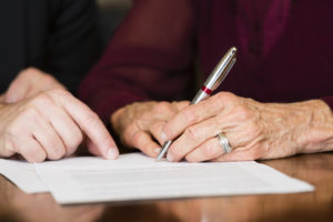 Estate planning attorney assisting elderly woman holding a pen with signing estate planning documents.