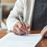 Cropped shot of an unrecognizable man sitting alone in his home and signing his will