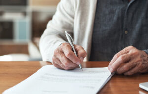 Cropped shot of an unrecognizable man sitting alone in his home and signing his will