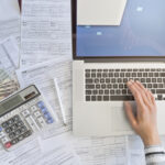 Close up photo of a woman doing taxes with laptop and tax forms in a house